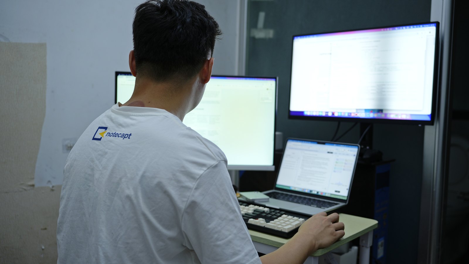 A second view of the same desk, code and documents open across three displays