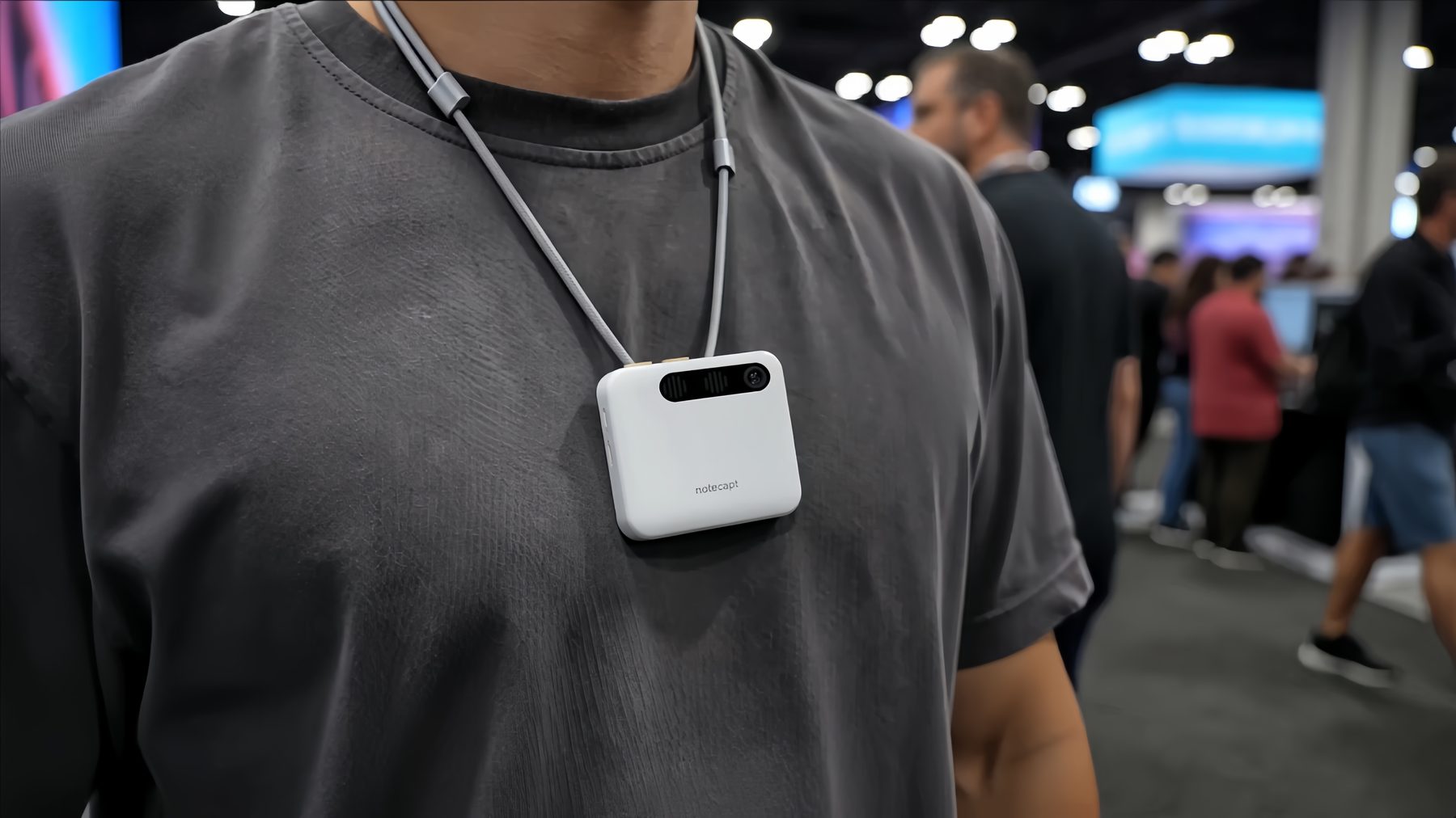 The A2 Pro worn on a neck lanyard against a grey T-shirt, on a trade show floor